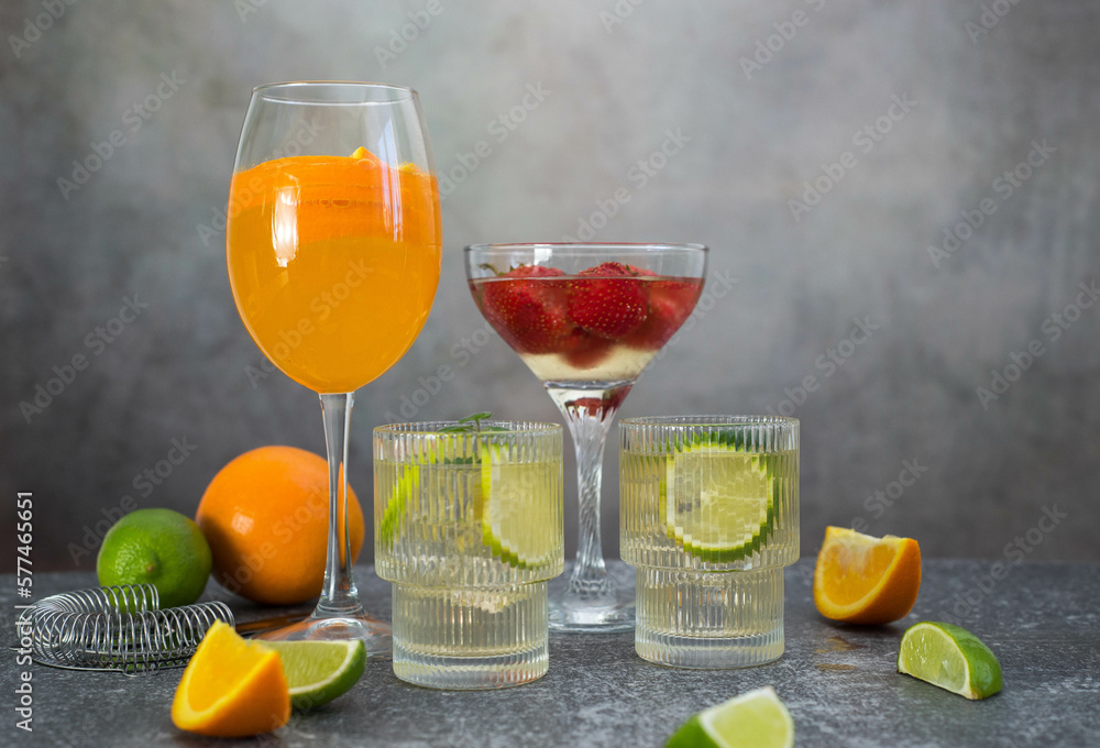assorted cocktails: two glasses of mojito, orange cocktail, cocktail with strawberries, fruits and shaker on a gray background.