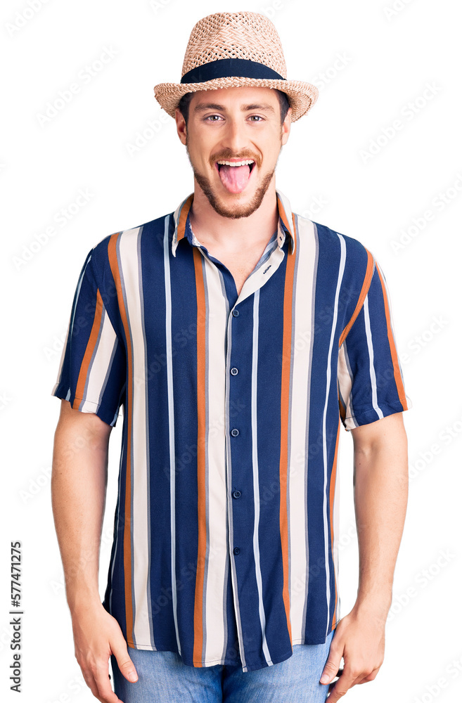 Young handsome caucasian man wearing summer hat sticking tongue out happy with funny expression. emotion concept. Young handsome caucasian man wearing summer hat sticking tongue out happy with funny expression. emotion concept.