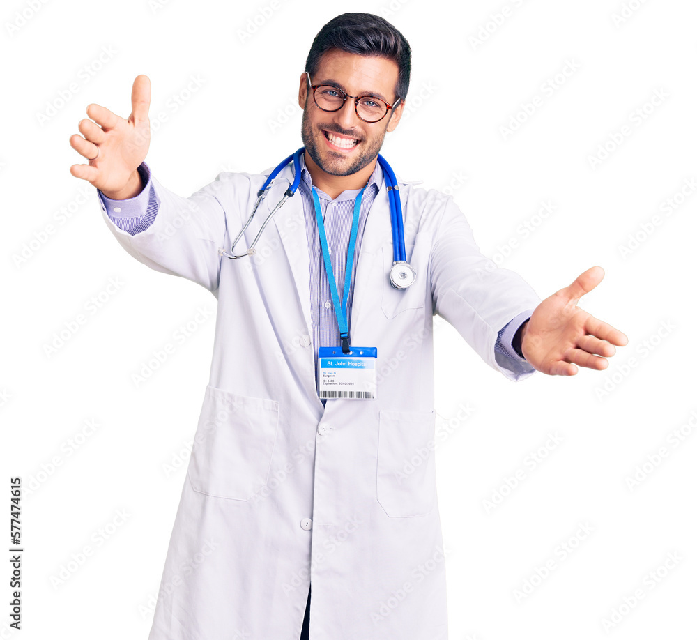 Young hispanic man wearing doctor uniform and stethoscope looking at the camera smiling with open arms for hug. cheerful expression embracing happiness. Young hispanic man wearing doctor uniform and stethoscope looking at the camera smiling with open arms for hug. cheerful expression embracing happiness.