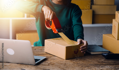 Startup SME small business entrepreneur of freelance Asian woman wearing apron using laptop and box to receive and review orders online to prepare to pack sell to customers, online sme business ideas.