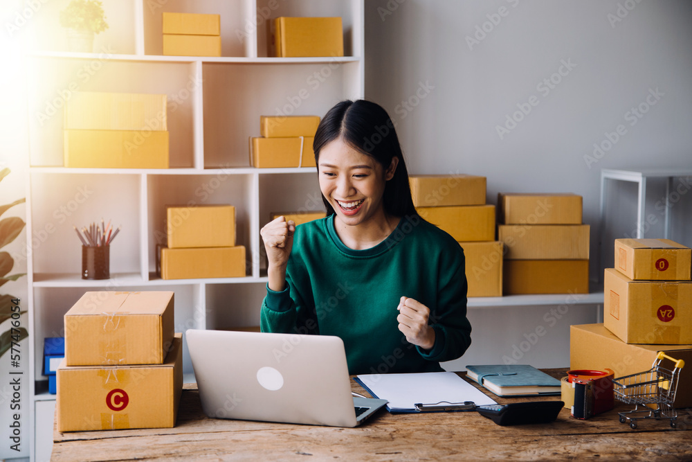 Startup SME small business entrepreneur of freelance Asian woman wearing apron using laptop and box to receive and review orders online to prepare to pack sell to customers, online sme business ideas. Startup SME small business entrepreneur of freelance Asian woman wearing apron using laptop and box to receive and review orders online to prepare to pack sell to customers, online sme business ideas.