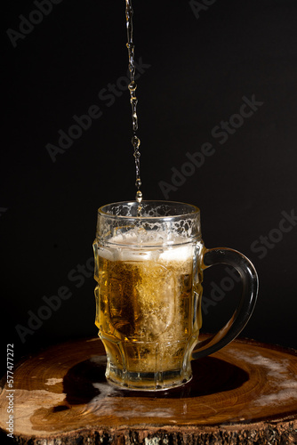 Sirviendo cerveza fría y espumosa en vaso cervecero sobre tronco de madera en fondo negro - serving cold foamy beer in pint glass on wooden log on black background