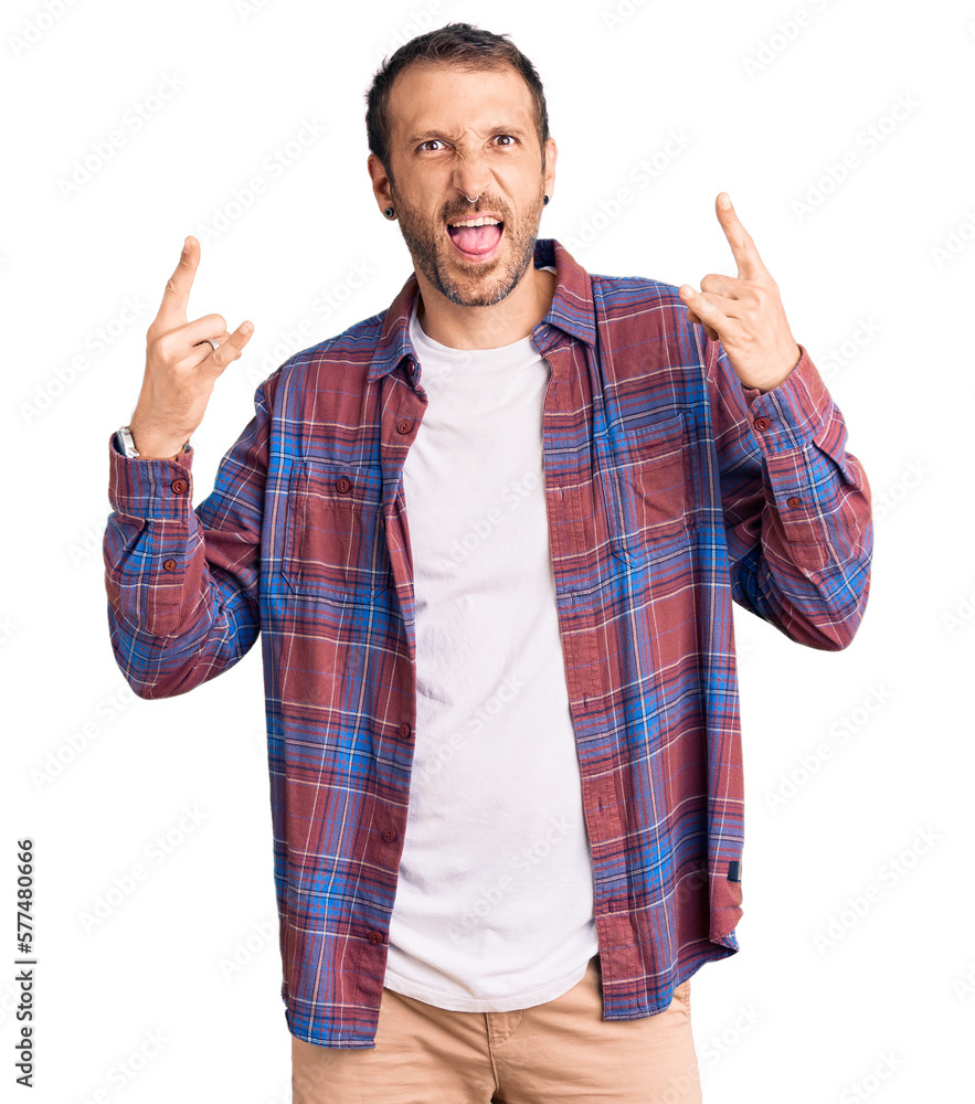 Young handsome man wearing casual clothes shouting with crazy expression doing rock symbol with hands up. music star. heavy music concept. Young handsome man wearing casual clothes shouting with crazy expression doing rock symbol with hands up. music star. heavy music concept.