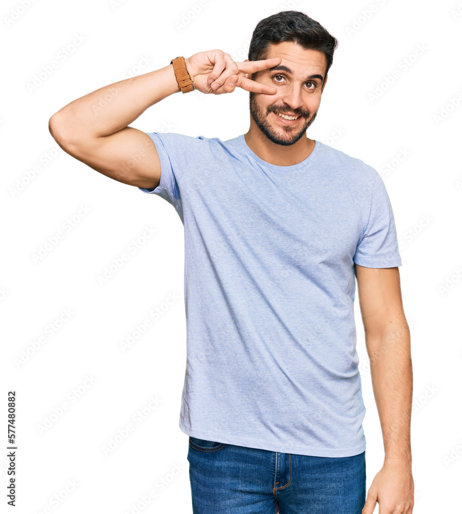 Young hispanic man wearing casual clothes doing peace symbol with fingers over face, smiling cheerful showing victory Young hispanic man wearing casual clothes doing peace symbol with fingers over face, smiling cheerful showing victory