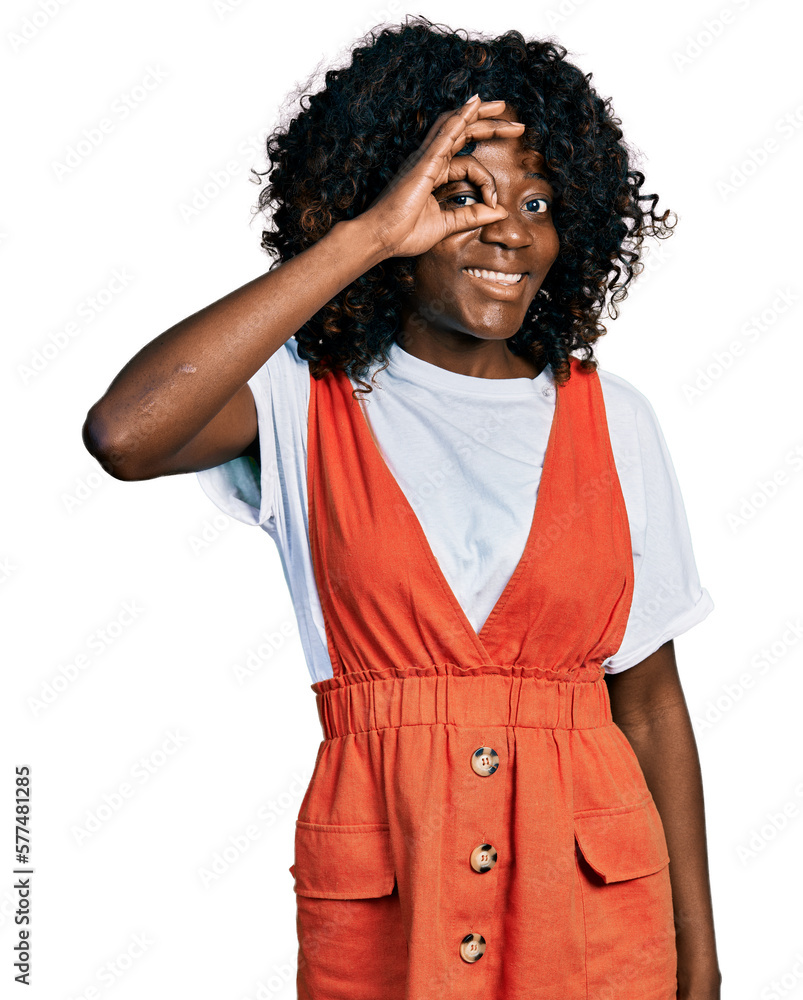 African woman with curly hair wearing casual white t shirt smiling happy doing ok sign with hand on eye looking through fingers