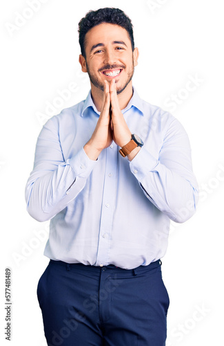 Young hispanic man wearing business clothes praying with hands together asking for forgiveness smiling confident. © Krakenimages.com