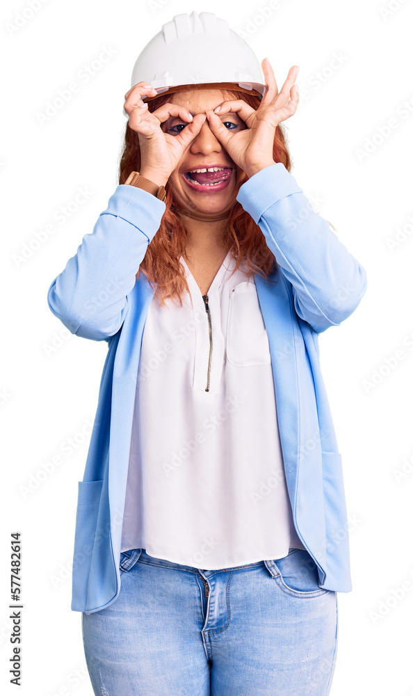 Young latin woman wearing architect hardhat doing ok gesture like binoculars sticking tongue out, eyes looking through fingers. crazy expression. Young latin woman wearing architect hardhat doing ok gesture like binoculars sticking tongue out, eyes looking through fingers. crazy expression.