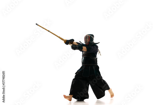 Man, professional kendo athlete in motion, in uniform training with bamboo sword, shinai against white studio background. Concept of martial arts, sport, Japanese culture, action and motion