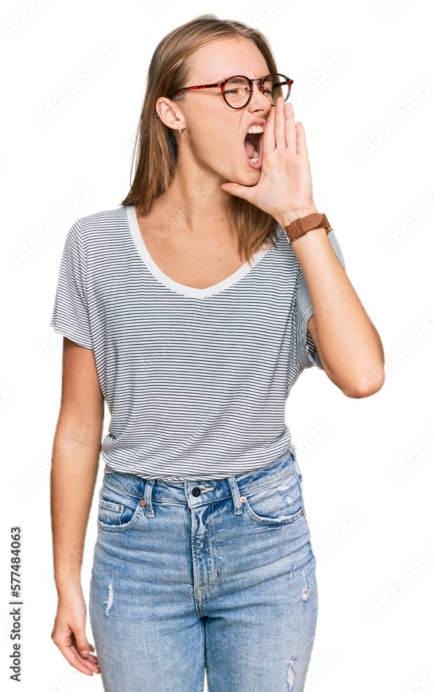 Beautiful young blonde woman wearing casual clothes and glasses shouting and screaming loud to side with hand on mouth. communication concept.