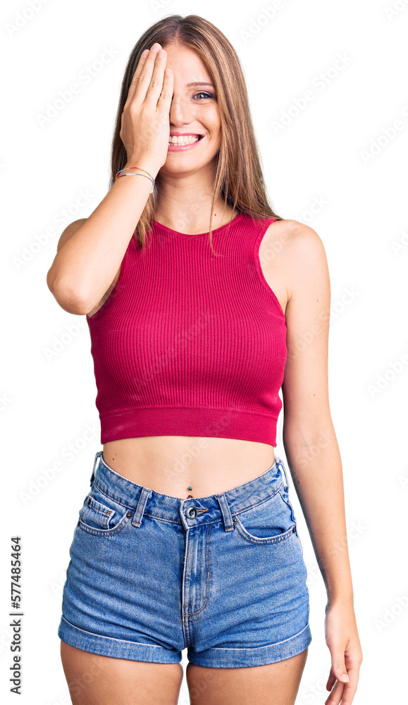 Young beautiful blonde woman wearing elegant summer shirt covering one eye with hand, confident smile on face and surprise emotion. Young beautiful blonde woman wearing elegant summer shirt covering one eye with hand, confident smile on face and surprise emotion.