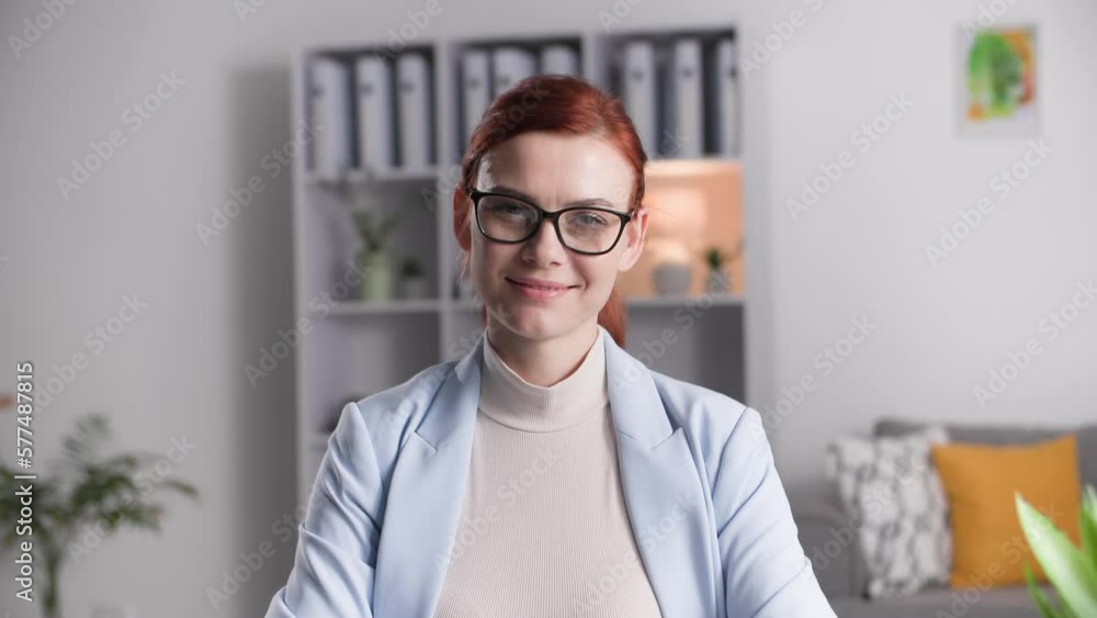 portrait of charming woman in glasses, works remotely on a computer while sitting in room, connects portable disk with data to laptop, smiles and looks at camera portrait of charming woman in glasses, works remotely on a computer while sitting in room, connects portable disk with data to laptop, smiles and looks at camera