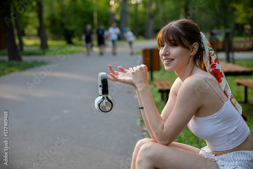 A smiling woman presents wireless headphones while holding them in her hand.