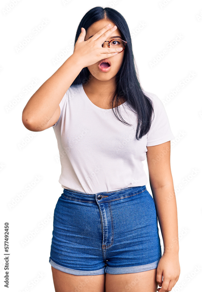 Young beautiful asian girl wearing casual clothes and glasses peeking in shock covering face and eyes with hand, looking through fingers with embarrassed expression. Young beautiful asian girl wearing casual clothes and glasses peeking in shock covering face and eyes with hand, looking through fingers with embarrassed expression.