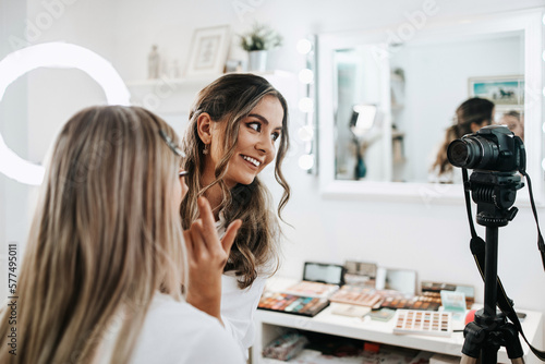 Happy young woman streaming a beauty makeup vlog from home or workshop. Beautiful online content creator cosmetician applying makeup and explaining some work tools. Vlogging and online channel work.
