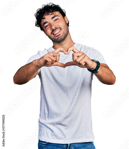 Hispanic young man with beard wearing casual white t shirt smiling in love doing heart symbol shape with hands. romantic concept.