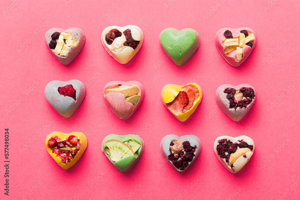 Fototapeta premium chocolate sweets in the form of a heart with fruits and nuts on a colored background. top view with space for text, holiday concept