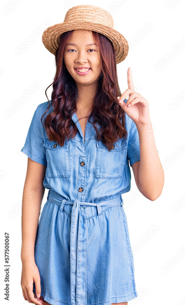Young beautiful chinese girl wearing summer hat showing and pointing up with finger number one while smiling confident and happy. Young beautiful chinese girl wearing summer hat showing and pointing up with finger number one while smiling confident and happy.