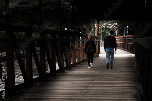 Neo noir man and woman crossing shadowy dark bridge boardwalk