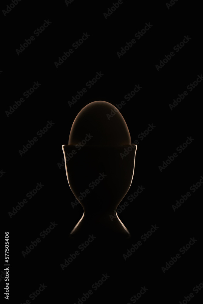 Dark Easter egg in a cup on black background with silhouette rim light and flare Dark Easter egg in a cup on black background with silhouette rim light and flare