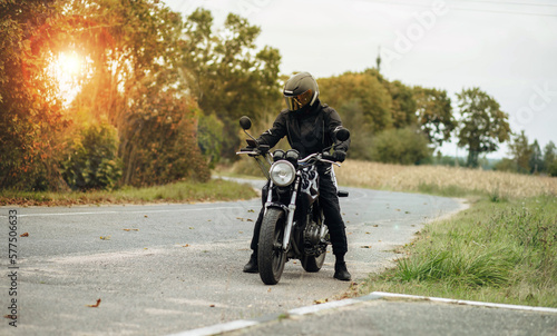 motorcyclist in motorcycle clothing and a helmet on an old motorcycle cafe racer in the summer on the road