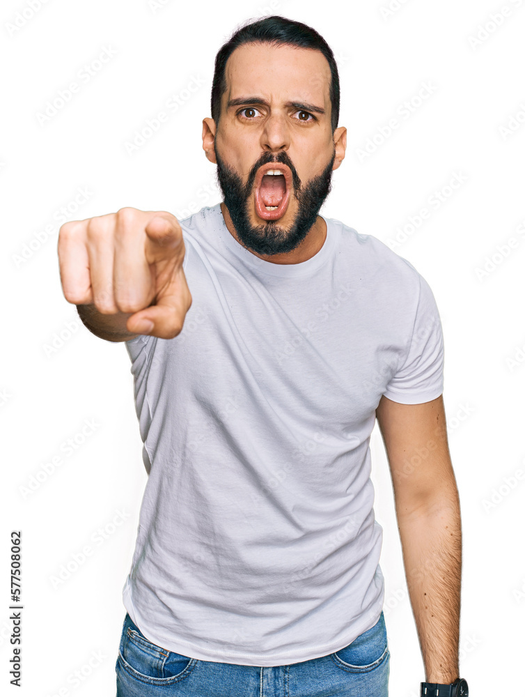 Young man with beard wearing casual white t shirt pointing displeased and frustrated to the camera, angry and furious with you Young man with beard wearing casual white t shirt pointing displeased and frustrated to the camera, angry and furious with you