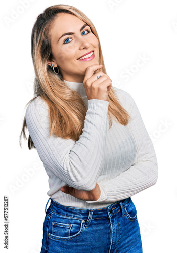 Young blonde woman wearing casual clothes smiling looking confident at the camera with crossed arms and hand on chin. thinking positive.