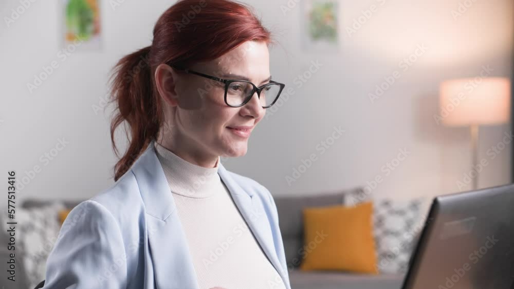 portrait of young female employee working remotely behind a laptop at home smiling and looking at camera portrait of young female employee working remotely behind a laptop at home smiling and looking at camera