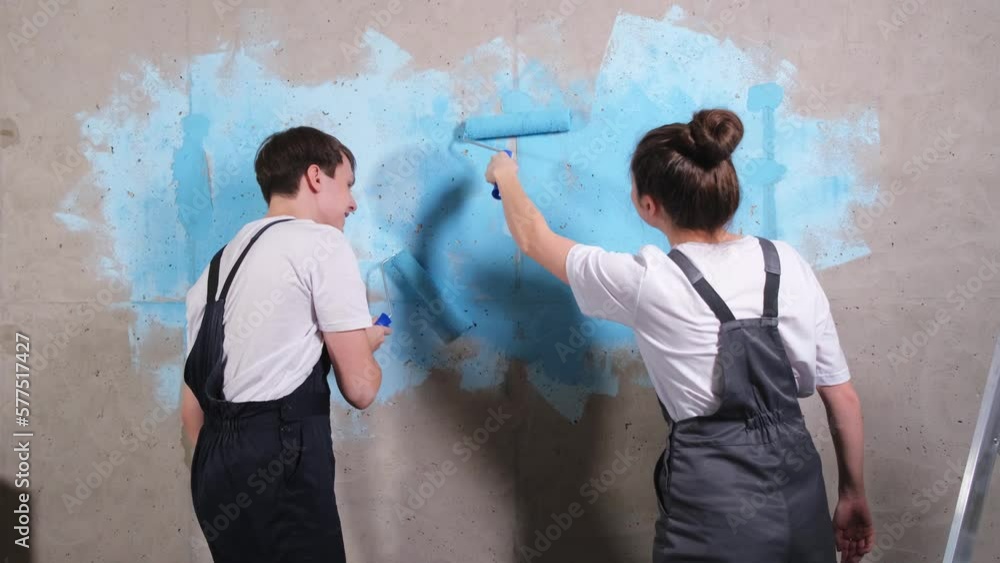 Couple in new home during repair works painting wall together. Happy family holding paint roller