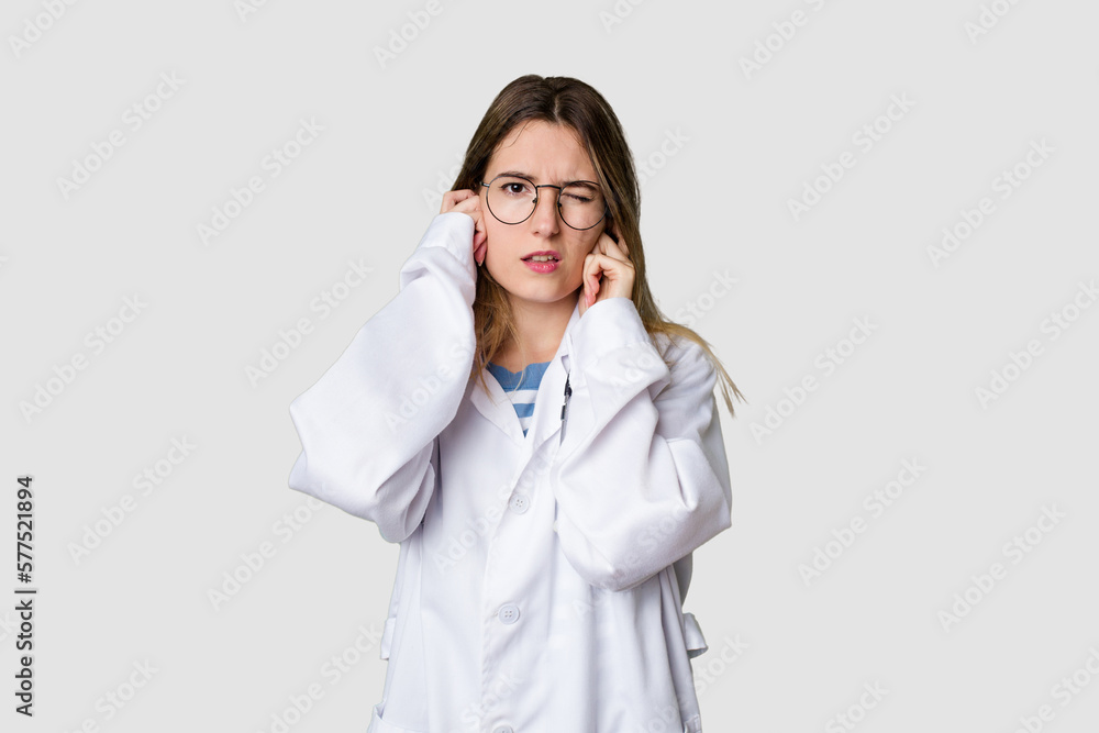 Compassionate female physician with a stethoscope around her neck, ready to diagnose and care for her patients in her signature white coat covering ears with hands.