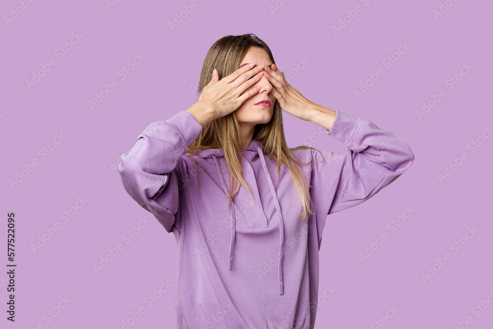 Young blonde posing for a portrait isolated, exuding natural beauty and radiance afraid covering eyes with hands. Young blonde posing for a portrait isolated, exuding natural beauty and radiance afraid covering eyes with hands.