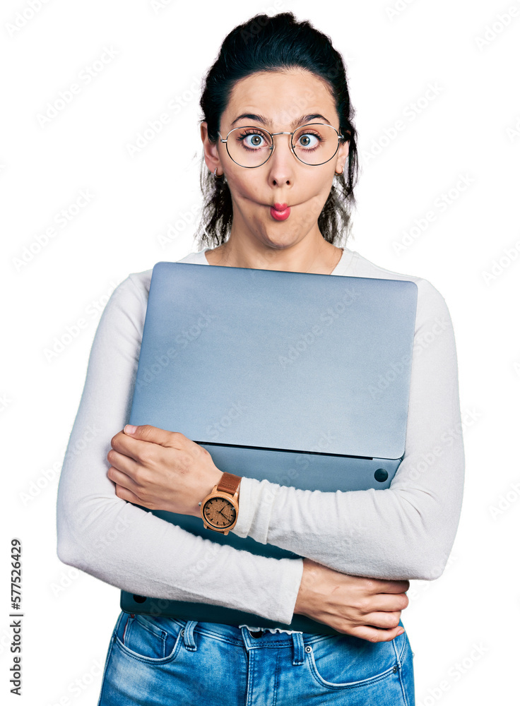 Young hispanic woman working using computer laptop making fish face with mouth and squinting eyes, crazy and comical. Young hispanic woman working using computer laptop making fish face with mouth and squinting eyes, crazy and comical.