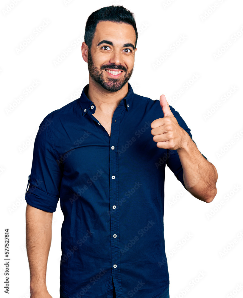 Young hispanic man with beard wearing casual blue shirt smiling happy and positive, thumb up doing excellent and approval sign Young hispanic man with beard wearing casual blue shirt smiling happy and positive, thumb up doing excellent and approval sign
