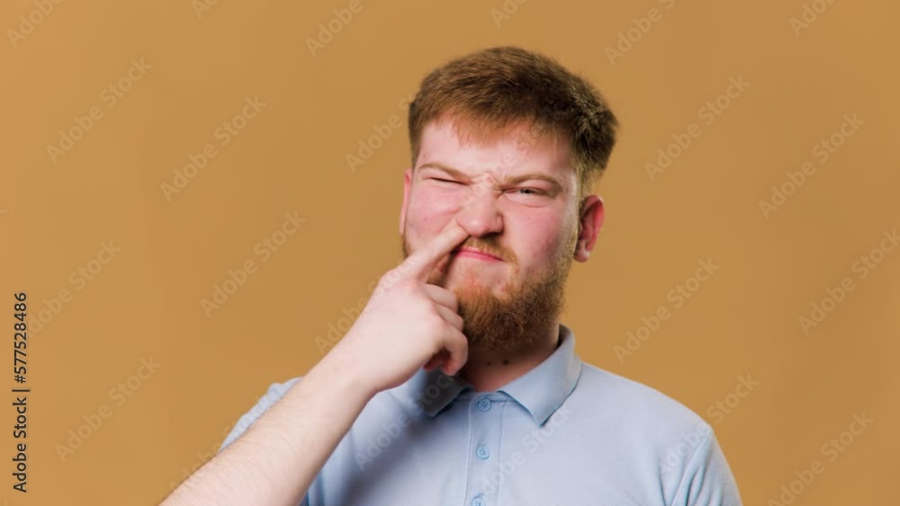 A funny studio shot of a redhead teenage guy with his finger in nose looking at camera A funny studio shot of a redhead teenage guy with his finger in nose looking at camera