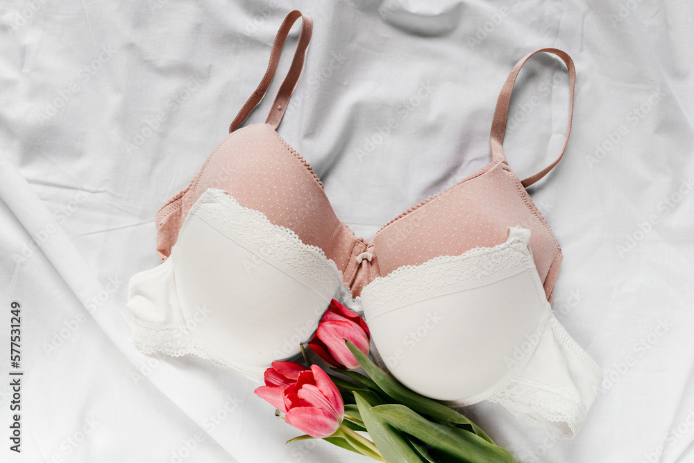 White and pink bras, pink tulips on the bed. Women tender lingerie,  underwear. Top view, close up. Flat lay, beauty blog or social media  minimal concept. Present for Valentines, Women's day Stock