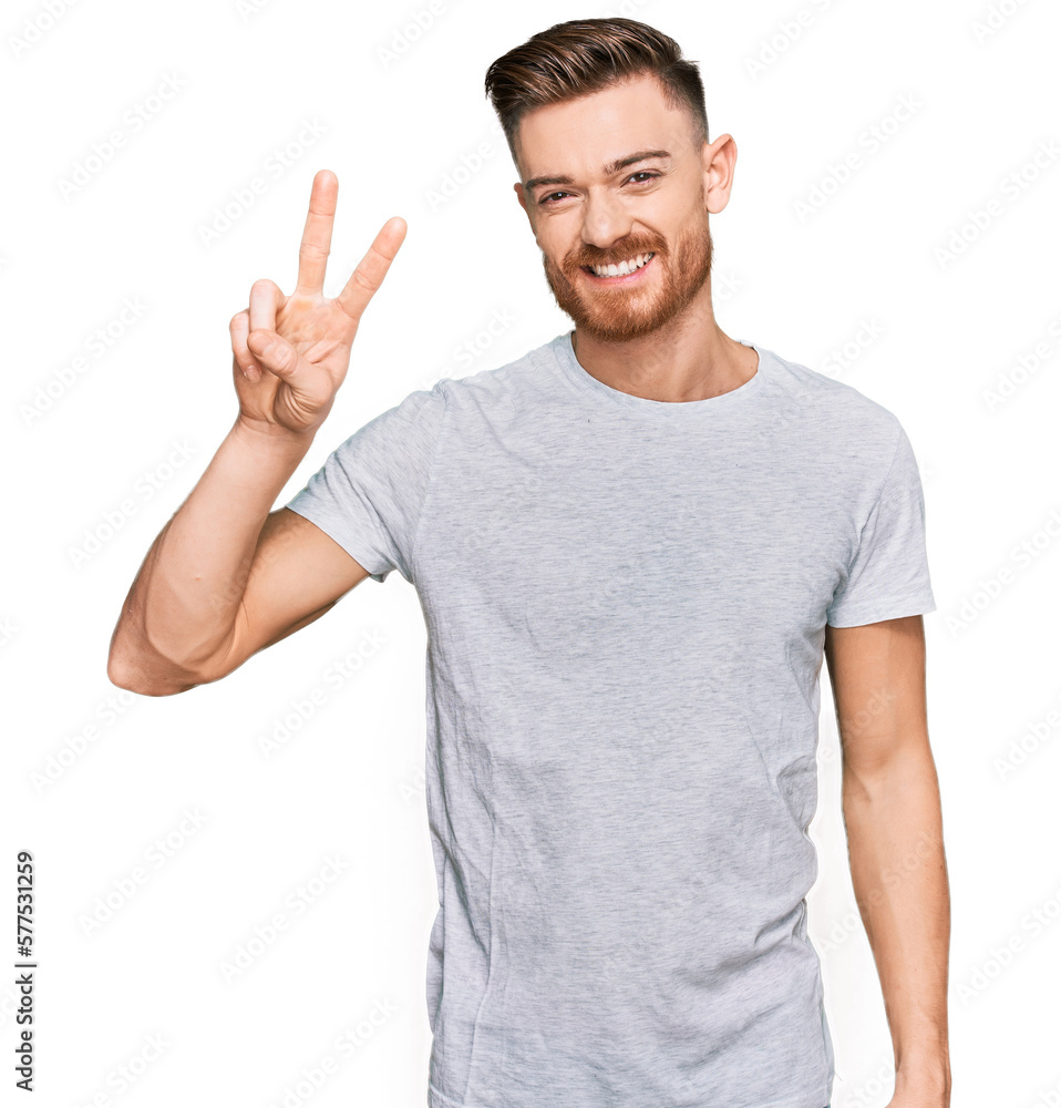 Young redhead man wearing casual grey t shirt showing and pointing up with fingers number two while smiling confident and happy. Young redhead man wearing casual grey t shirt showing and pointing up with fingers number two while smiling confident and happy.