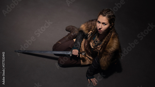A young brave Viking heroine gazing up sitting on the floor. A young woman in a suit in Scandinavian or fantasy style