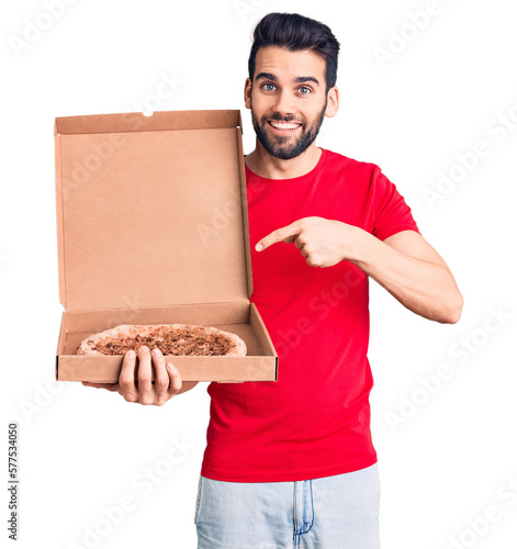 Young handsome man with beard holding delivery cardoboard with italian pizza smiling happy pointing with hand and finger photo