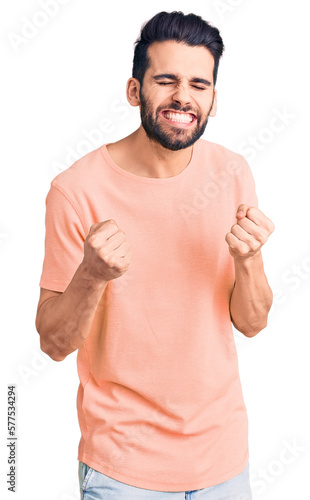 Young handsome man with beard wearing casual t-shirt excited for success with arms raised and eyes closed celebrating victory smiling. winner concept.