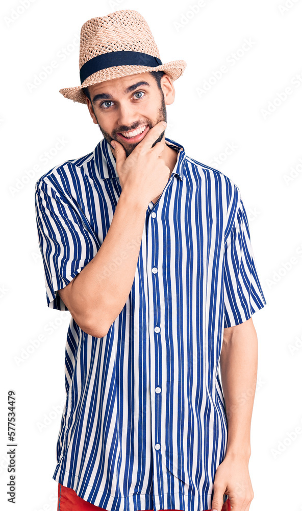 Young handsome man with beard wearing summer hat and striped shirt looking confident at the camera smiling with crossed arms and hand raised on chin. thinking positive. Young handsome man with beard wearing summer hat and striped shirt looking confident at the camera smiling with crossed arms and hand raised on chin. thinking positive.