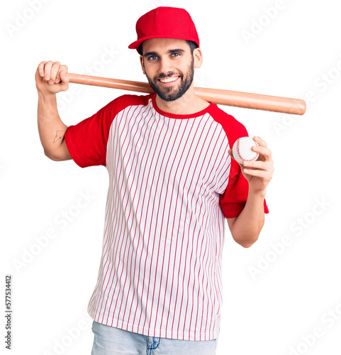 Young handsome man with beard playing baseball holding bat and ball looking positive and happy standing and smiling with a confident smile showing teeth