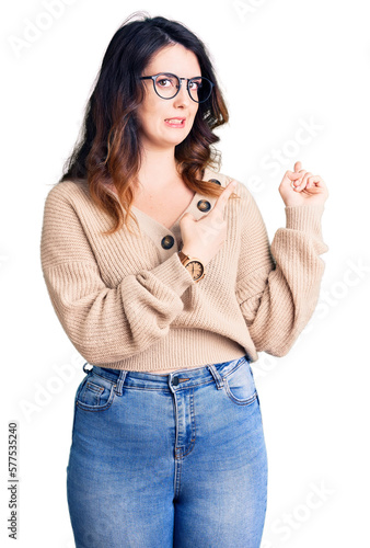 Beautiful young brunette woman wearing casual clothes and glasses pointing aside worried and nervous with both hands, concerned and surprised expression