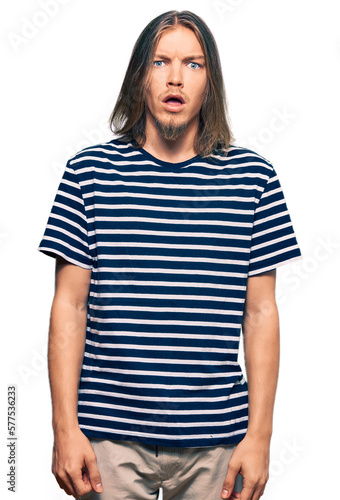 Handsome caucasian man with long hair wearing casual striped t-shirt afraid and shocked with surprise expression, fear and excited face.