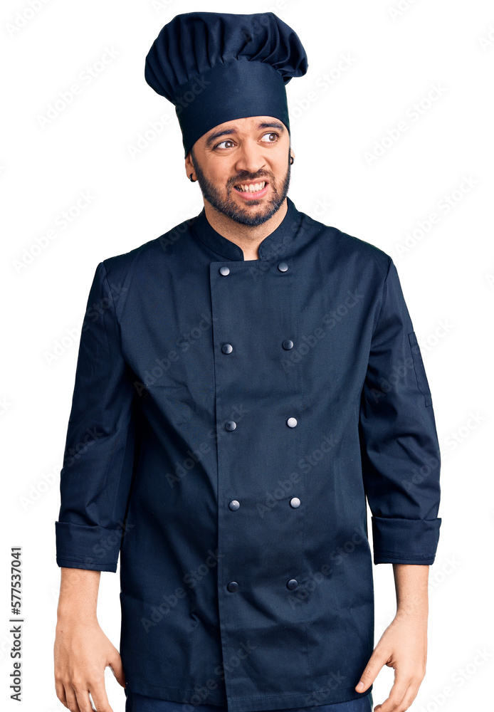 Young hispanic man wearing cooker uniform looking away to side with smile on face, natural expression. laughing confident.