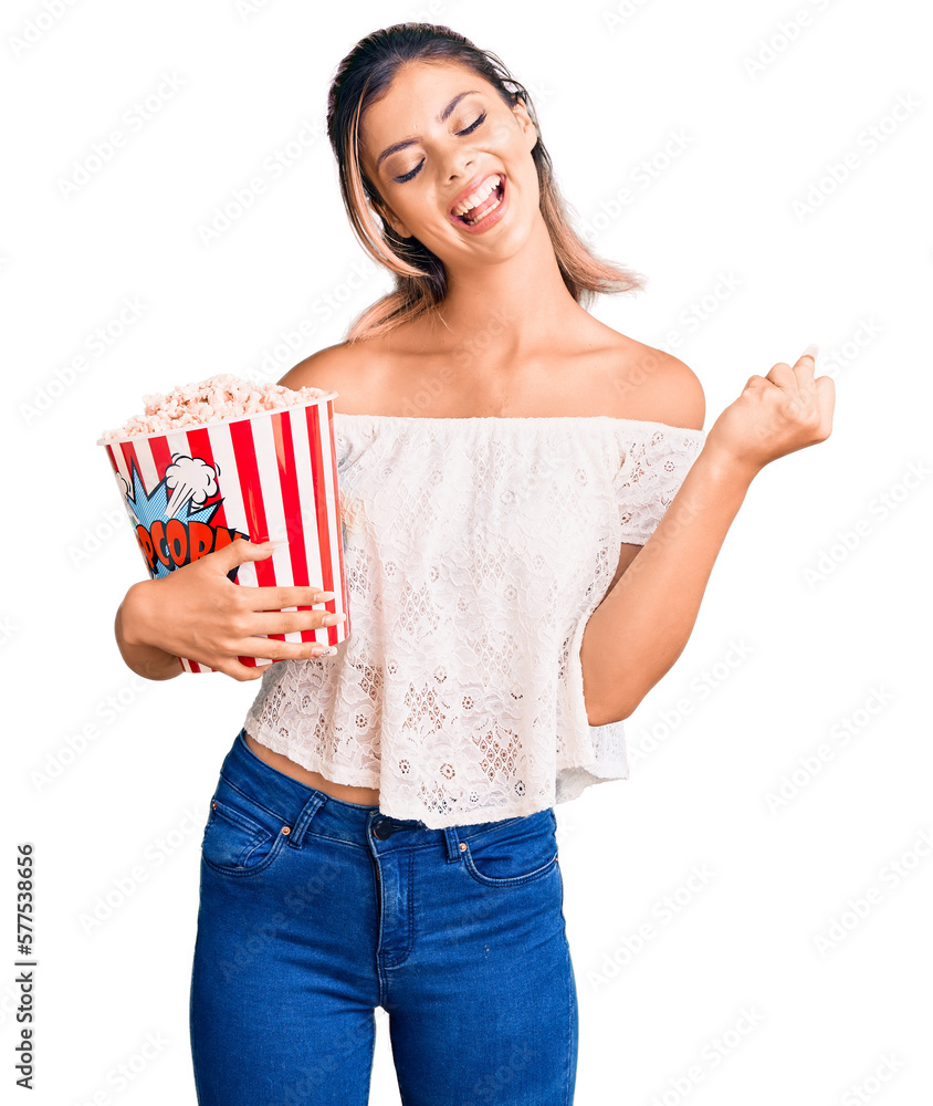 Young beautiful woman holding popcorn screaming proud, celebrating victory and success very excited with raised arms Young beautiful woman holding popcorn screaming proud, celebrating victory and success very excited with raised arms