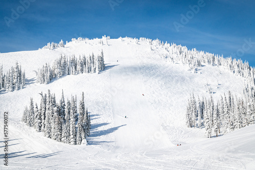 Fototapeta Naklejka Na Ścianę i Meble -  Photo of 3 skiers heading down a widely groomed trail on the mountain from mid-mountain at a ski resort in the Columbia Mountain range in British Columbia, Canada.