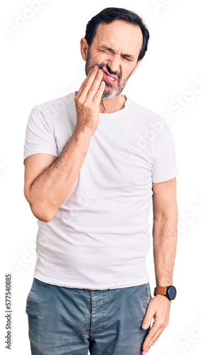 Middle age handsome man wearing casual t-shirt touching mouth with hand with painful expression because of toothache or dental illness on teeth. dentist