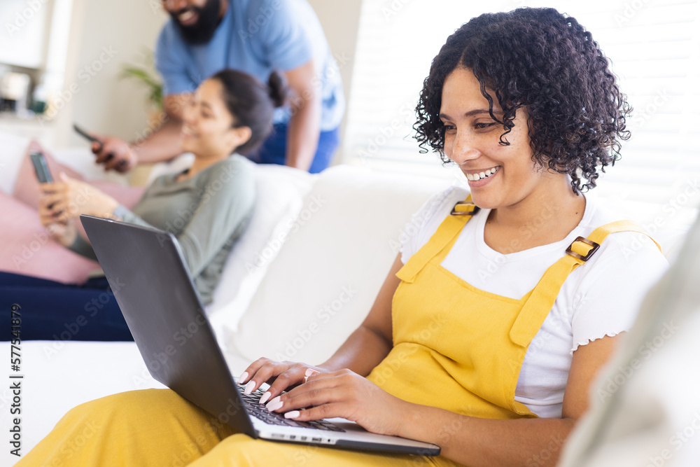 Happy diverse friends sitting on sofa, using electronic devices Happy diverse friends sitting on sofa, using electronic devices