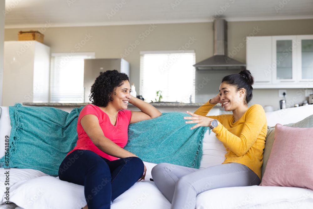 Happy biracial female friends sitting on sofa and talking Happy biracial female friends sitting on sofa and talking