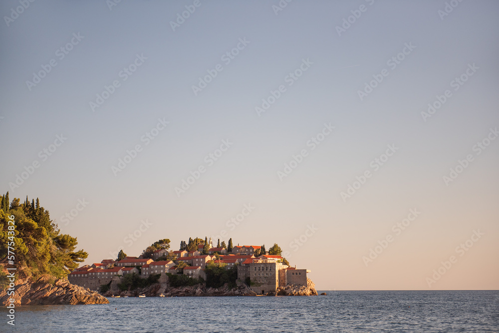 Panoramic view of Sveti Stefan in Montenegro at pink sunset. Famous tourist place near Budva. Natural beautiful island, with terracotta roofs among the turquoise sea. Copy space, wallpaper background