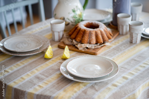 Easter lemon bundt cake, Babka sprinkled with powdered sugar on a festive table decorated with ceramic dishes. Rustic, Scandinavian style in table setting for a holiday, gray yellow linen tablecloth